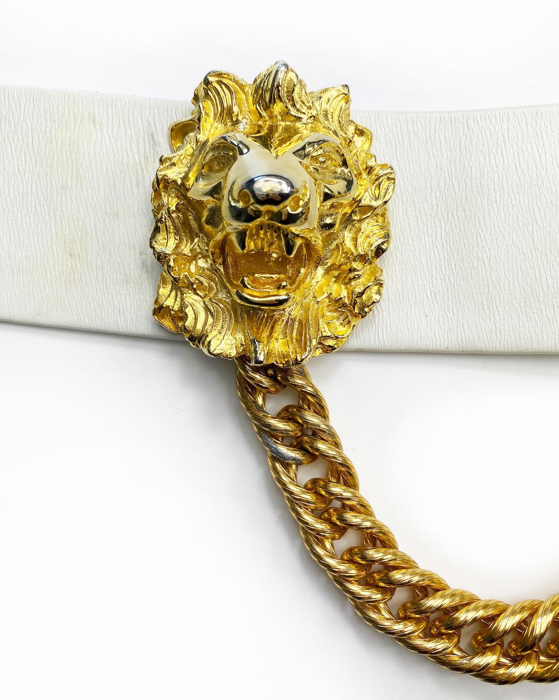 Fruit Vintage iconic Judith Leiber lion head belt with drop chains. This piece is amazing! It features 3 very large gold tone metal lions heads with drop chains on a white leather belt.