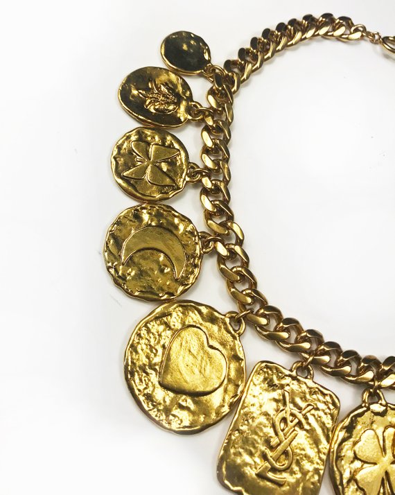 Fruit Vintage rare 1980s Yves Saint Laurent 'lucky charm' medallion necklace with textured logo. It features heavy gold plating in a deep yellow tone and various iconic YSL symbols such as the moon, clover, heart and bird.