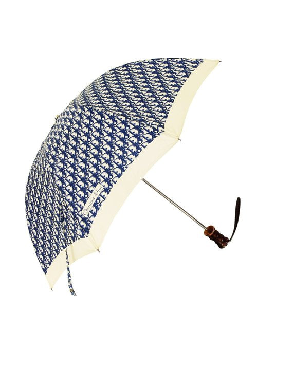 FRUIT vintage Christian Dior navy oblique logo umbrella dating to the late 1970s-early 1980s. This compact umbrella is in working condition with a matching cover, features the classic Christian Dior trotter/oblique print all over, Christian Dior logo text, telescoping stick and faux wood handle.