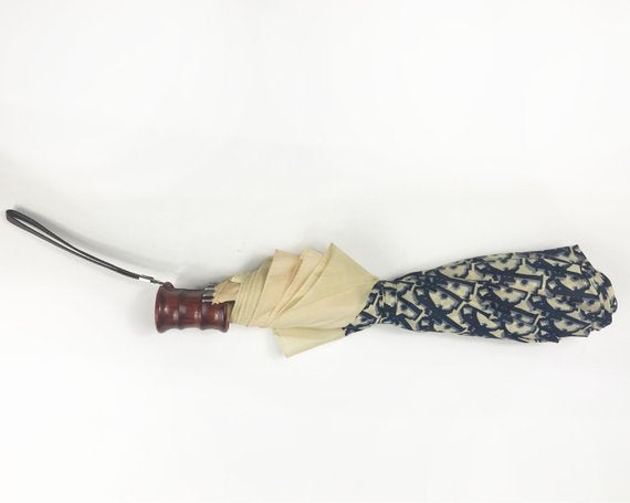 FRUIT vintage Christian Dior navy oblique logo umbrella dating to the late 1970s-early 1980s. This compact umbrella is in working condition with a matching cover, features the classic Christian Dior trotter/oblique print all over, Christian Dior logo text, telescoping stick and faux wood handle.