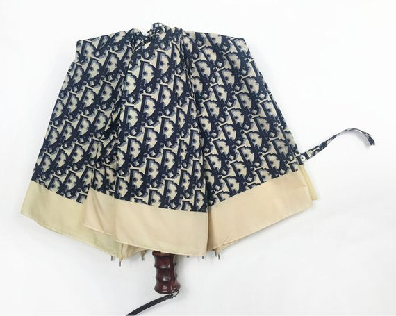 FRUIT vintage Christian Dior navy oblique logo umbrella dating to the late 1970s-early 1980s. This compact umbrella is in working condition with a matching cover, features the classic Christian Dior trotter/oblique print all over, Christian Dior logo text, telescoping stick and faux wood handle.