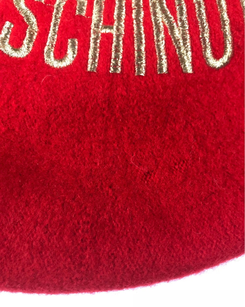 FRUIT Vintage Moschino logo beret hat. It features large embroidered gold text with the slogal "Moschinon Moschinoff" and a classic beret hat shape.