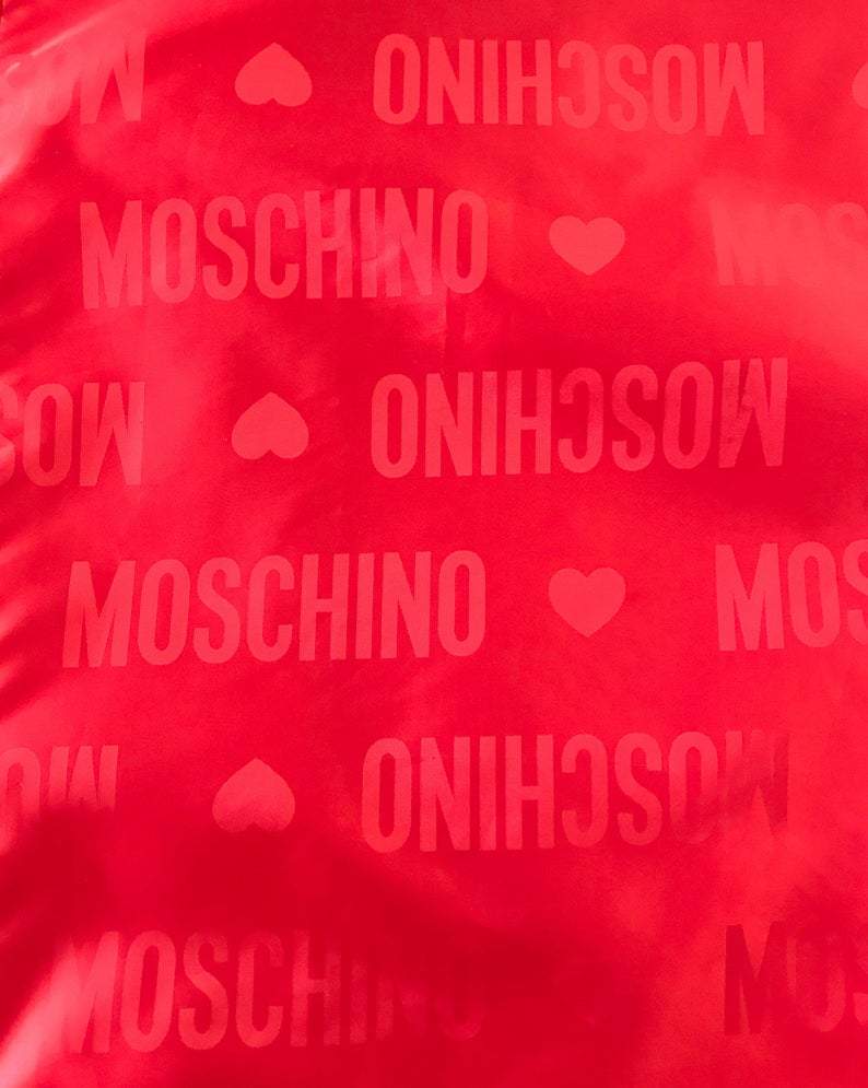 FRUIT Vintage red Moschino Cheap & Chic logo raincoat dating to the 1990s. It features large Moschino logo print all over, heart shaped button closure, front pockets and tie belt.