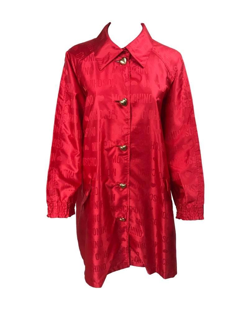 FRUIT Vintage red Moschino Cheap & Chic logo raincoat dating to the 1990s. It features large Moschino logo print all over, heart shaped button closure, front pockets and tie belt.