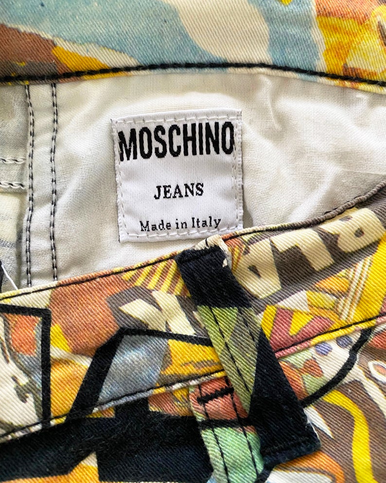 FRUIT Vintage Moschino cartoon print jeans dating to the early 1990s. They feature a classic mid-waist cut with a soft stretch denim and the incredible custom 90s Moschino logo print all over