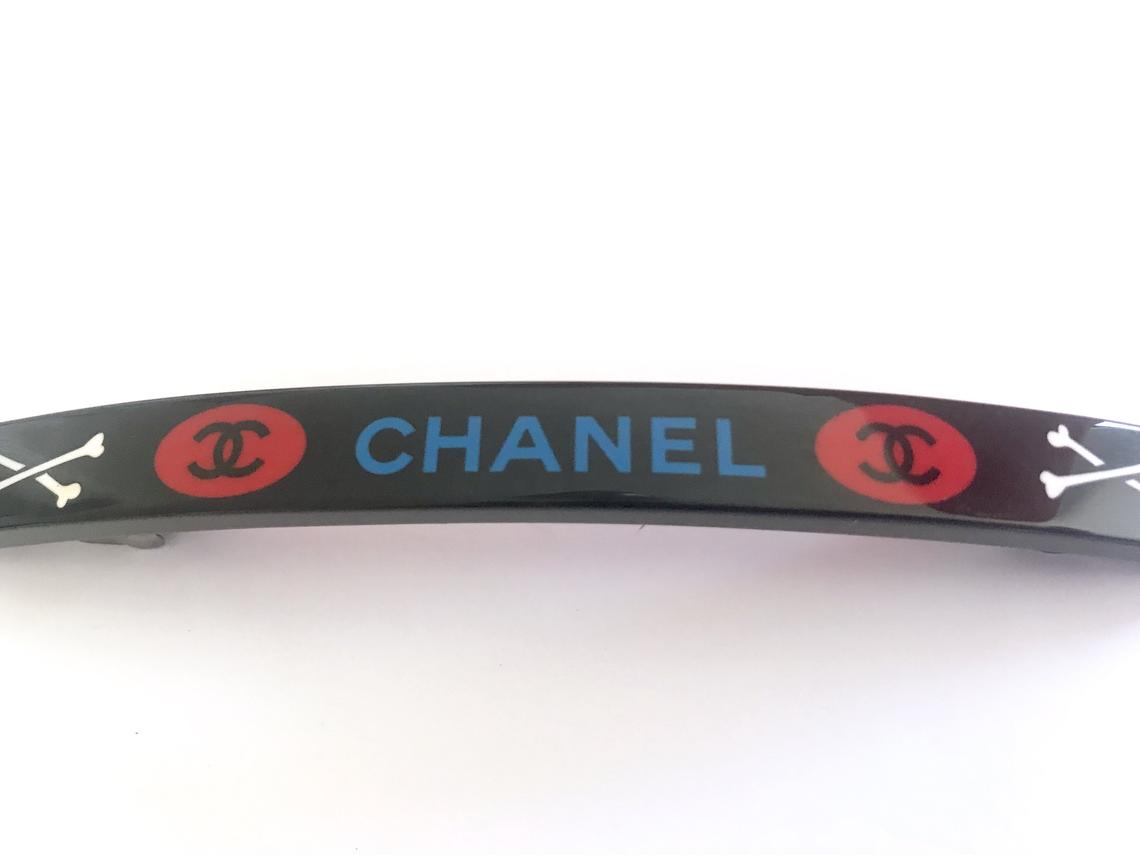 Fruit Vintage Chanel 2003 text logo barrette in black with cross bones. Features large Chanel text logos and two CC monograms either side.