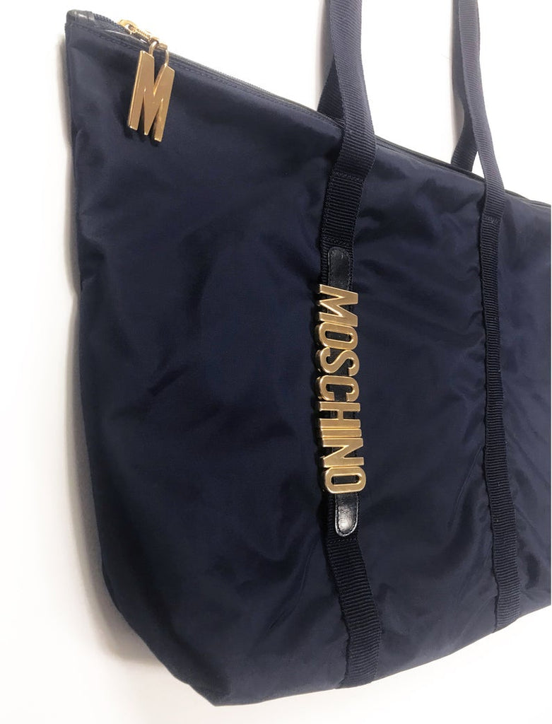 FRUIT Vintage Moschino tote bag with the iconic Moschino gold lettering to one side. The tote is very roomy and fits a large amount, perfect for use as a shopping tote or beach bag. Features an internal zipper pocket along with a zipped internal attached pouch, Moschino logo lining, Moschino Redwall authenticity stamp and logo plaque at rear.