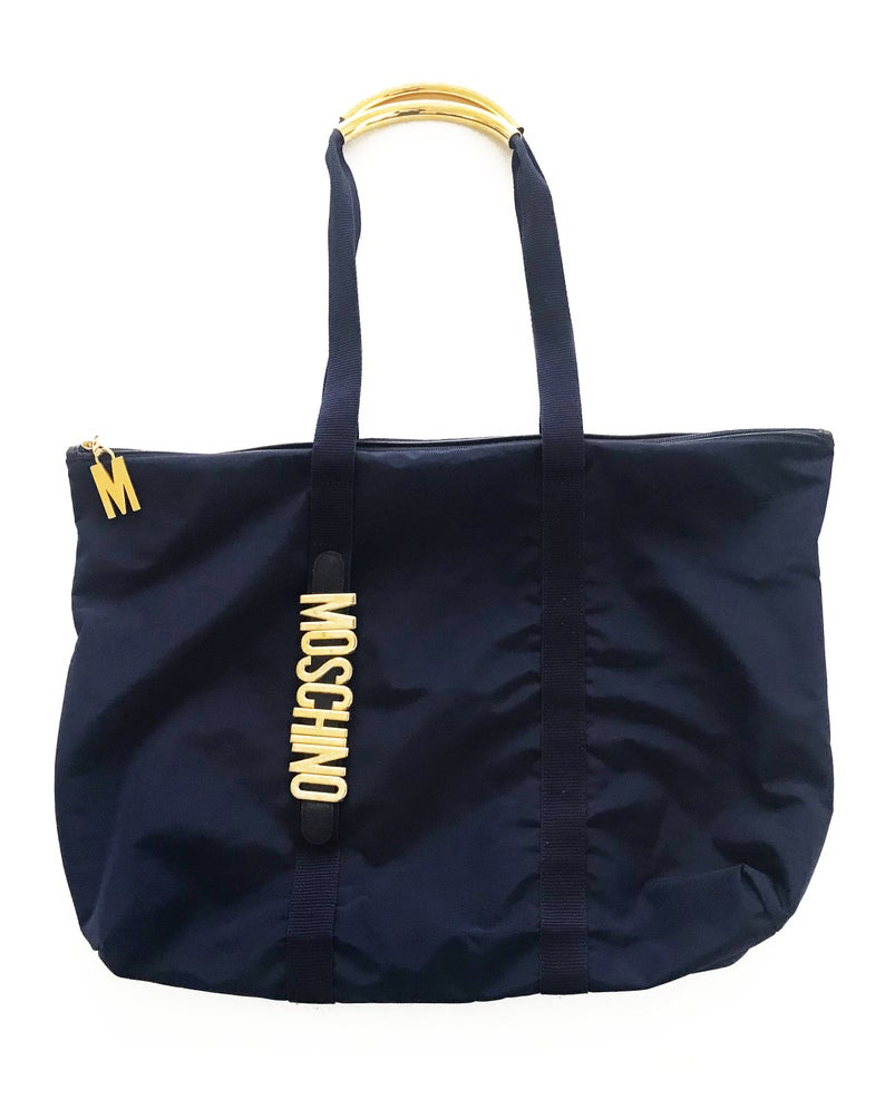 FRUIT Vintage Moschino tote bag with the iconic Moschino gold lettering to one side. The tote is very roomy and fits a large amount, perfect for use as a shopping tote or beach bag. Features an internal zipper pocket along with a zipped internal attached pouch, Moschino logo lining, Moschino Redwall authenticity stamp and logo plaque at rear.