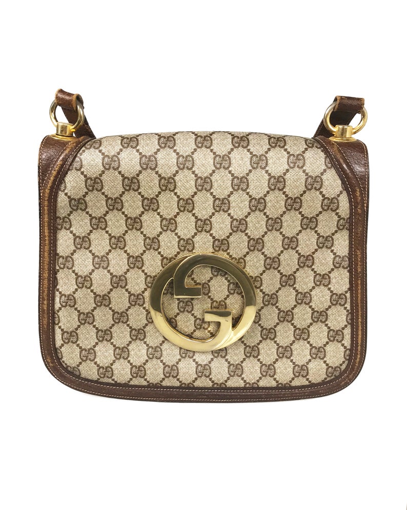 The 1973 Blondie bag is one of the most iconic Gucci styles!  This gorgeous shoulder bag features a very large front double G Gucci Logo at the front, a classic flap closure, brown leather trim and internal zipper pocket.