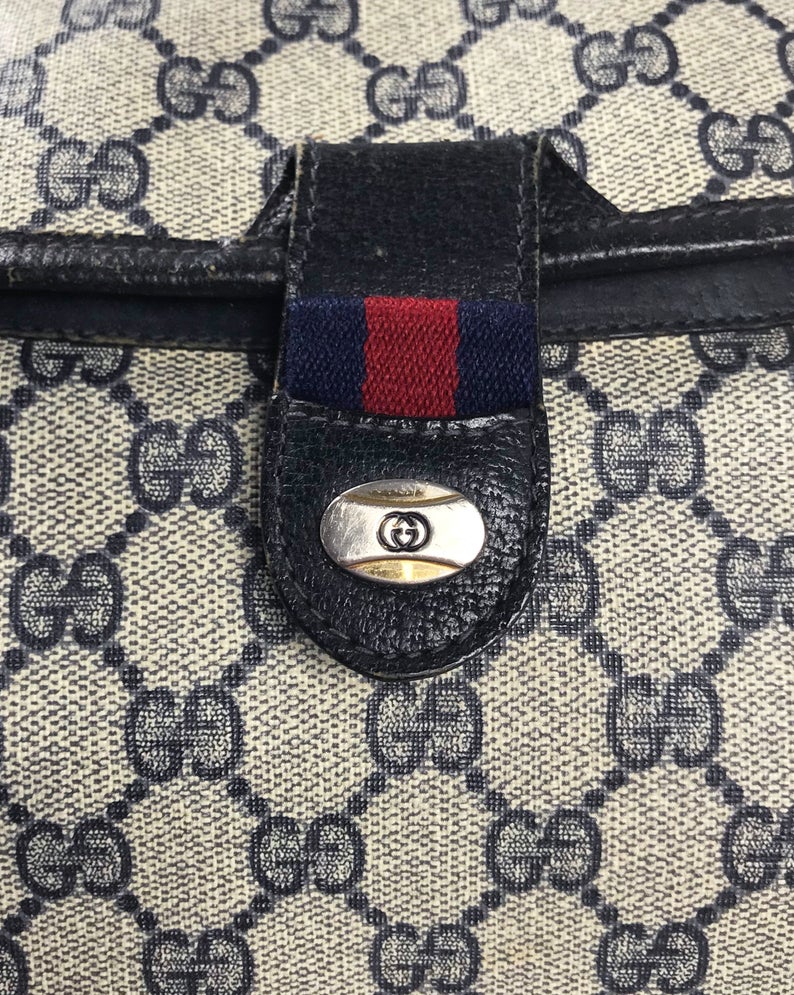 FRUIT Vintage Gucci 1980s logo clutch bag in a navy coated Gucci monogram canvas. It features a classic gucci navy and red racing stripe front detail, internal zipper pocket and separated pockets.