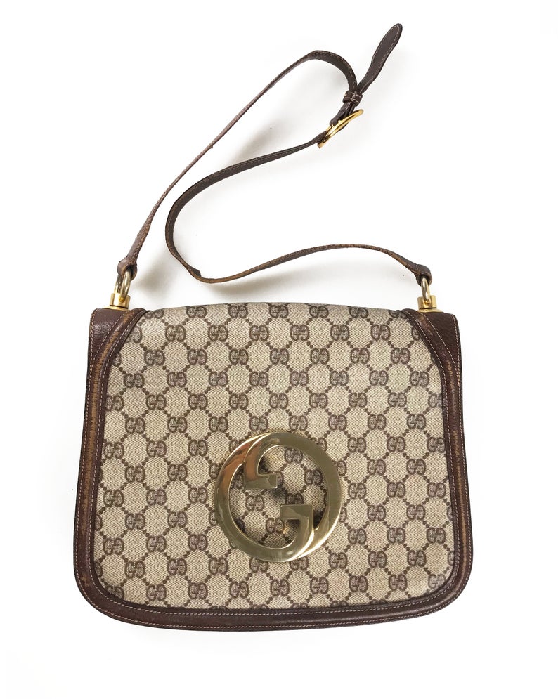 The 1973 Blondie bag is one of the most iconic Gucci styles!  This gorgeous shoulder bag features a very large front double G Gucci Logo at the front, a classic flap closure, brown leather trim and internal zipper pocket.