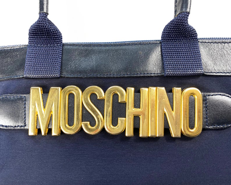 FRUIT Vintage Moschino mini tote bag with the iconic Moschino gold lettering at front. Features a top zipper closure with M logo zipper pull, Moschino logo lining, Moschino Redwall authenticity stamp and logo plaque at side.