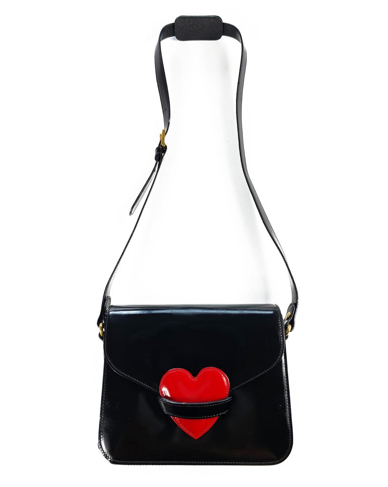 FRUIT Vintage rare Moschino heart cross body handbag in a classic satchel shape. Features an internal zipper pocket, Moschino logo lining, magnetic button front closure, Moschino Redwall authenticity stamp and logo plaque at side.